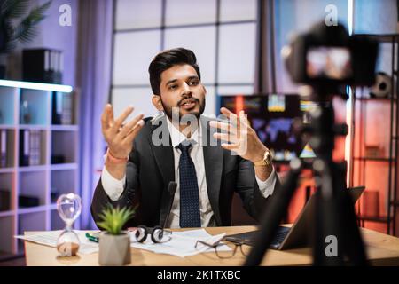 Ritratto di attraente sicuro esperto indiano intelligente bearded Office manager registrazione video vlog per il pubblico di Internet in ufficio serale. Foto Stock