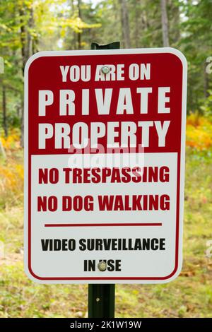 Un cartello di proprietà privata rosso e bianco avverte che non vi sono trasgressamenti, non vi sono camminate con cani e videosorveglianza in uso. Foto Stock