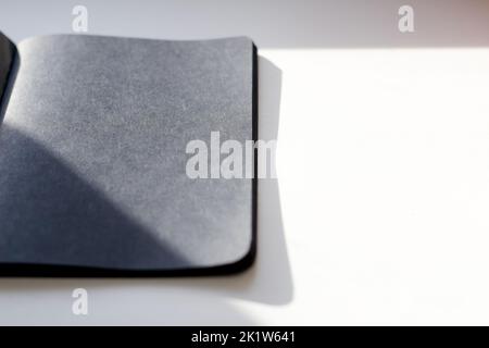 Sfocate un notebook nero vuoto su un tavolo bianco, foto mockup. Modello di copertina nero vuoto con spazio di copia per la progettazione. Design minimalista nero. Shad Foto Stock