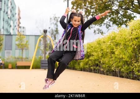 Ragazza sorridente che oscilla su una corda in un parco giochi Foto Stock