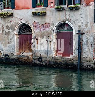 Primo piano di un'antica facciata di un vecchio edificio colorato con porte e finestre su un canale con riflessione d'acqua a Venezia. Foto Stock