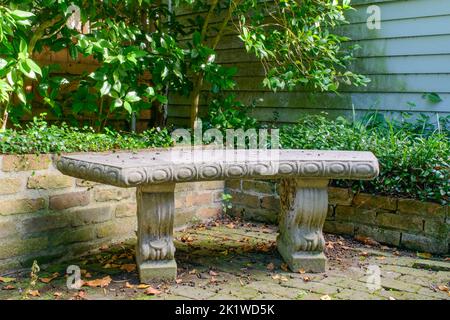 Primo piano di panca giardino in cemento sul patio in mattoni della storica casa di New Orleans Foto Stock