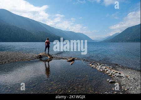 Giovane donna che gode di vista sulla riva del lago Crescent nel Parco Nazionale Olimpico, Washington nel soleggiato pomeriggio autunnale. Foto Stock