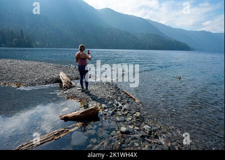 Giovane donna che gode di vista sulla riva del lago Crescent nel Parco Nazionale Olimpico, Washington nel soleggiato pomeriggio autunnale. Foto Stock