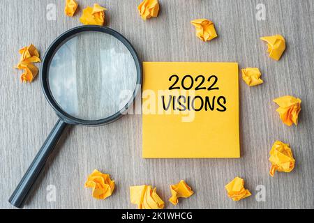 2022 VISIONI parole su nota gialla con carta sbriciolata e lente d'ingrandimento su sfondo tavolo di legno. Nuovo anno nuovo inizio, idea, strategia e obiettivi c Foto Stock