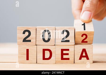 Mano di businessman che tiene cubo di legno e capovolgere blocco 2021 a 2022 IDEA su sfondo tavolo. Risoluzione, piano, tendenza, cambiamento, inizio e Capodanno ho Foto Stock