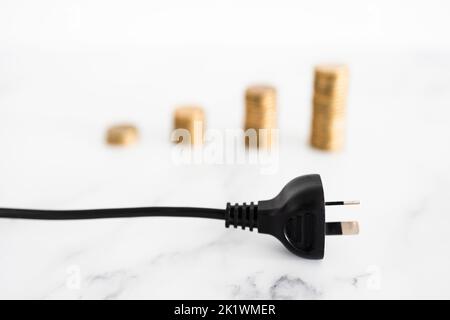 i costi dell'elettricità aumentano l'immagine concettuale, si inseriscono con pile crescenti di monete nel backgroung che rappresentano i prezzi che aumentano Foto Stock