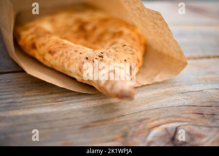 Una tortilla cotta a mano si trova in un sacchetto di carta su un tavolo di legno. Kraft. Pane nazionale. Imballaggio ecologico. Cibo biologico. Foto Stock