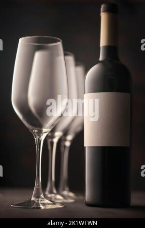 bicchieri da vino e una bottiglia di vino rosso con etichetta bianca senza iscrizione. Bella vita soulful, sfondo scuro atmosfera atmosfera. Foto Stock