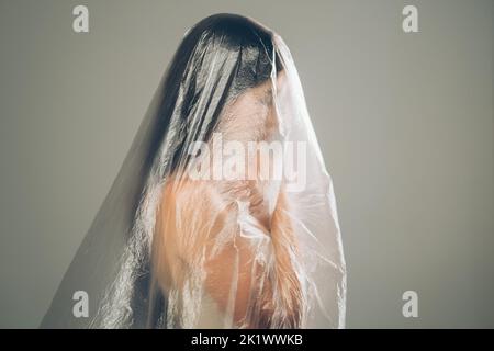 Discriminazione femminile. Ritratto sfocato. Sicurezza di protezione. Profilo di donna imbarazzata insicura coperta con pellicola trasparente di polietilene isolato Foto Stock