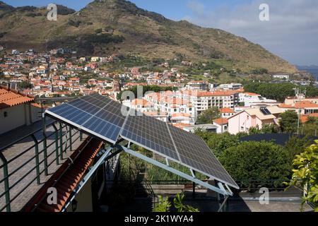 Pannelli solari su abitazioni domestiche a Machico, Madeira orientale, con la città oltre Foto Stock