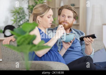 coppia incinta che mangia cereali davanti alla tv Foto Stock