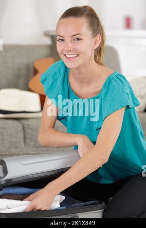 donna felice che incolli vestiti in valigia Foto Stock