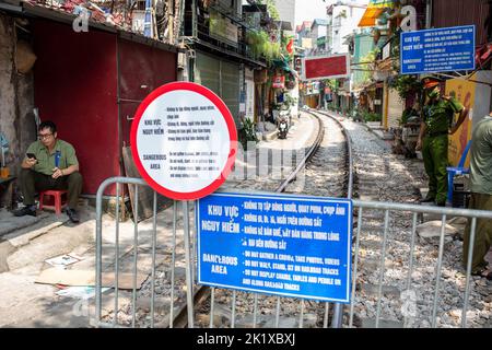 19 settembre 2022, Vietnam, Hanoi: Gli agenti di polizia sorvegliano le barriere alla "strada dei treni", ancora una volta chiusa. Solo pochi mesi dopo la riapertura della famosa "strada dei treni", le autorità hanno chiuso nuovamente la vista. Dopo che l'accesso era stato vietato tre anni fa per motivi di sicurezza, i caffè e le bancarelle lungo il percorso ferroviario, che scorre tra piccoli blocchi di case, si erano riaperti sulla scia delle visite Corona - attirando visitatori da tutto il mondo. In un primo momento, la città ha lasciato i turisti in. Alcuni giorni fa, tuttavia, ha posto barriere con grandi segnali di avvertimento. Foto: Chris Humphre Foto Stock