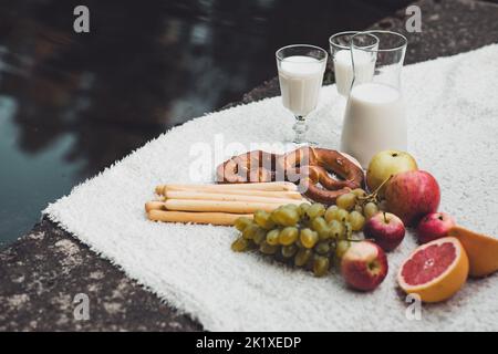 Cibo sano ecologico, dieta biologica, bicchieri da latte, salsiccia, pretzel, mela, pompelmo su coperta vicino al lago nel parco Cibo sano ecologico, dieta biologica, bicchieri da latte, salsiccia, pretzel, mela, pompelmo su coperta vicino al lago nel parco
