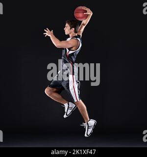 SCHIAFFO dunk. Profilo a tutta lunghezza di un giovane giocatore di basket maschile in azione su sfondo nero. Foto Stock