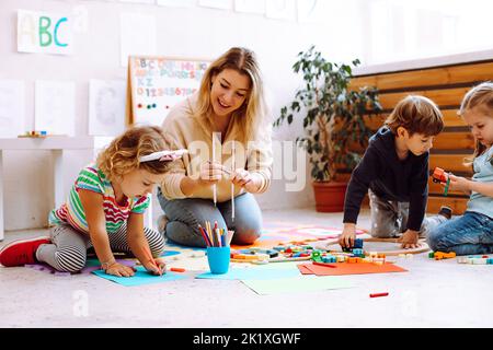 Sorridente insegnante giocare con i bambini, fare artigianato, colorate arti fatte a mano in centro di sviluppo per bambini speciali. Foto Stock