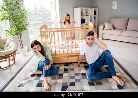 Full size ritratto di famiglia piena stanchi genitori sedersi tappeto pavimento eccitato ragazza hanno divertimento urlo dormire casa bambino al coperto Foto Stock