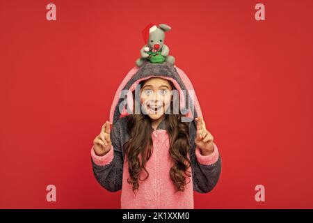 sorprendo il capretto nel pajama comodo tiene il giocattolo di natale su sfondo rosso, homewear Foto Stock