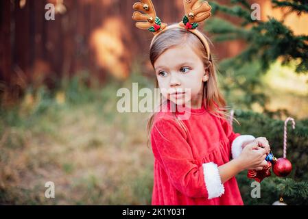 Natale nel mese di luglio. Bambino in attesa di Natale in legno nel mese di luglio. Ritratto di bambina decorazione albero di natale. Vacanze invernali e concetto di persone. Buon Natale e buone feste. Foto Stock