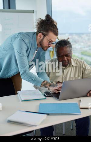 Un insegnante sta aiutando uno studente senior multiculturale a risolvere un problema di programmazione. Foto Stock