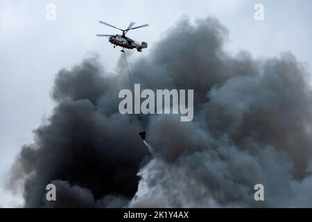 Un elicottero antincendio trasporta un contenitore d'acqua per spegnere un incendio in un edificio di produzione Foto Stock