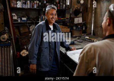 Ritratto di una donna sorridente che parla con un collega in un workshop industriale mentre si discute del progetto Foto Stock