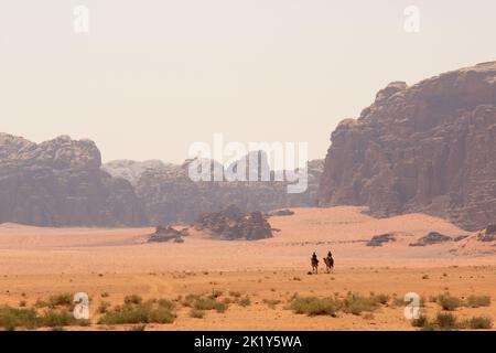 Vista spettacolare di due beduini in sella a cammelli nell'iconico deserto di Wadi Rum, in Giordania. Foto Stock