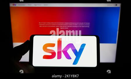 Persona che detiene uno smartphone con il logo della società di media britannica Sky Group Limited sullo schermo davanti al sito Web. Messa a fuoco sul display del telefono. Foto Stock