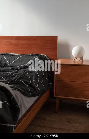 decorazioni interne di una camera da letto con letto in legno e comodino adornato con una trapunta e una lampada, mobili in stile minimalista Foto Stock