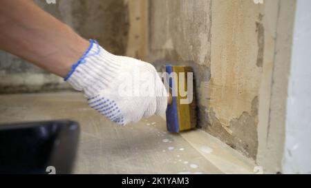 Primo piano, mani che tengono una spazzola, un lavoratore applica il primer bianco alla parete. Casa-pittore, mano tiene un pennello, disegna e innescato un muro. Il concetto di Foto Stock
