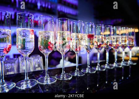 Una fila di bicchieri con ciliegie e champagne al banco del bar durante la preparazione di cocktail alcolici Foto Stock