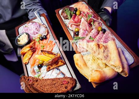 Il cameriere tiene un piatto di legno con varie prelibatezze secche a fette Foto Stock