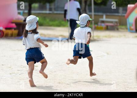 I bambini corrono a terra durante una giornata di sport in un asilo giapponese pre-scuola Foto Stock