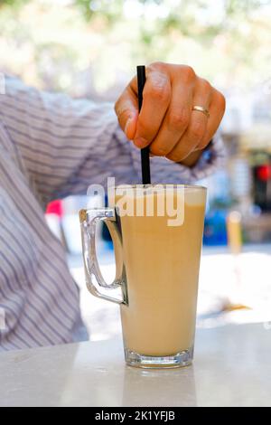 Caffè latte ghiacciato con una cannuccia sul tavolo. Foto Stock