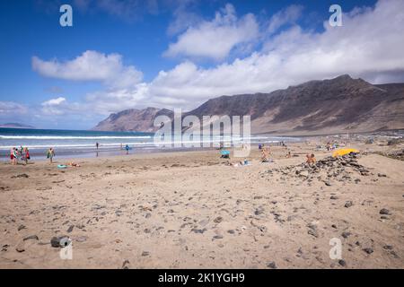 Lanzarote, SPAGNA - 14 settembre 2022: Spiaggia di Famara sull'isola di Lanzarote, Spagna. Persone che fanno il bagno sulla spiaggia. In acqua surfisti. Foto Stock