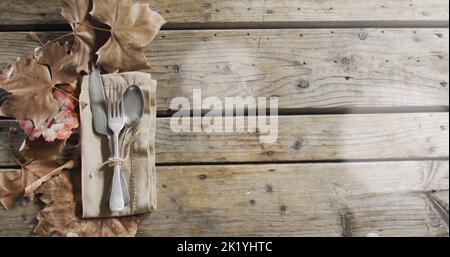 Immagine di macchie di luce su posate e foglie su sfondo di legno Foto Stock