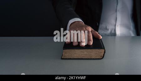 Mano sul libro nero , giurando sulla bibbia , concetto di dire la verità . su sfondo grigio blu . Foto Stock