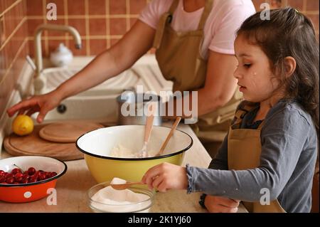 Vita domestica. Ragazza carina che prepara l'impasto con la madre nella cucina di casa. Concetto culinario e di cottura Foto Stock