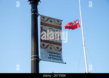 Un banner per l'Assemblea legislativa dell'Ontario è visto su un post al Queens Park con la bandiera dell'Ontario che sventola sullo sfondo. Foto Stock