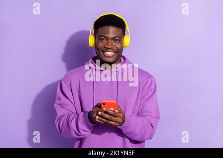 Ritratto di allegro amico uomo tenere telefono toothy sorriso godere playlist isolato su sfondo di colore viola Foto Stock