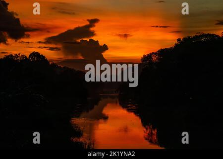 Gli alberi sono coperti di oscurità e la natura ha creato una splendida serata quando i colori rosso scuro, giallo e nero sono illuminati nelle nuvole. Foto Stock