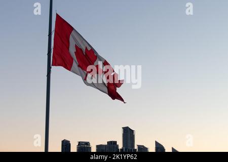Una grande bandiera canadese è vista al mattino presto in una giornata limpida, vicino a uno skyline moderno. Foto Stock