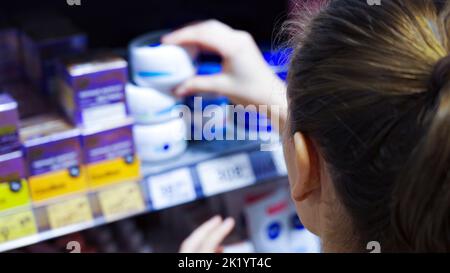Una giovane donna sceglie una crema cosmetica in un supermercato Foto Stock