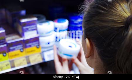 Una giovane donna sceglie una crema cosmetica in un supermercato Foto Stock