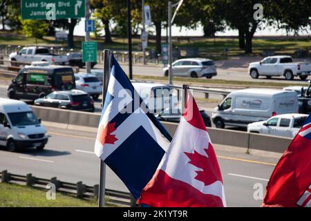 La bandiera della città di Toronto e la bandiera canadese si vedono sventolare in una giornata di sole accanto a una vivace Gardiner Expressway nel centro di Toronto. Foto Stock