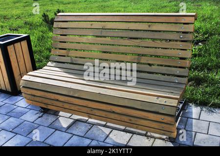 Panca in legno chiaro e urna in primo piano nel parco cittadino. Architettura urbana. Foto Stock