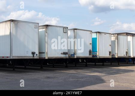 Una fila di rimorchi bianchi per il trasporto è allineata all'esterno di un magazzino in una giornata di sole e poco nuvolosa. Foto Stock