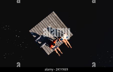 Uomo e donna seduti sul bordo della piattaforma di nuoto sul lago in estate. Foto Stock