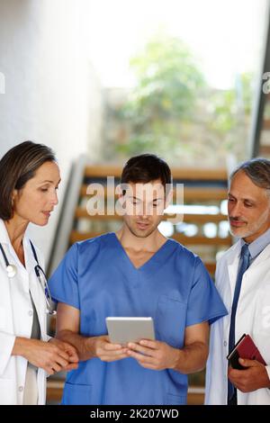 Accesso rapido alla storia clinica di un paziente. Una foto ritagliata di un bel giovane medico che mostra ai suoi colleghi alcune informazioni sul suo tablet. Foto Stock